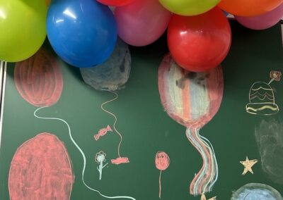 Rengarenk balonlar ve balon, çiçek ve yıldız çizimleriyle dolu bir tahta. Canlı renkler neşeli bir atmosfer yaratıyor.